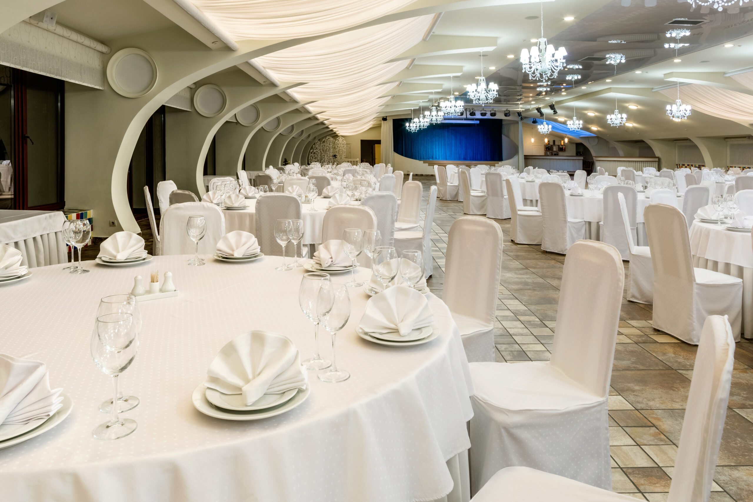 Banquet hall decorated in white with round served tables and sta